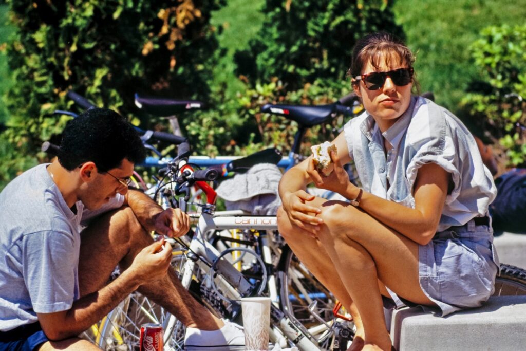 two Cornellians sit near a row of bikes on campus in a vintage color image from 1991