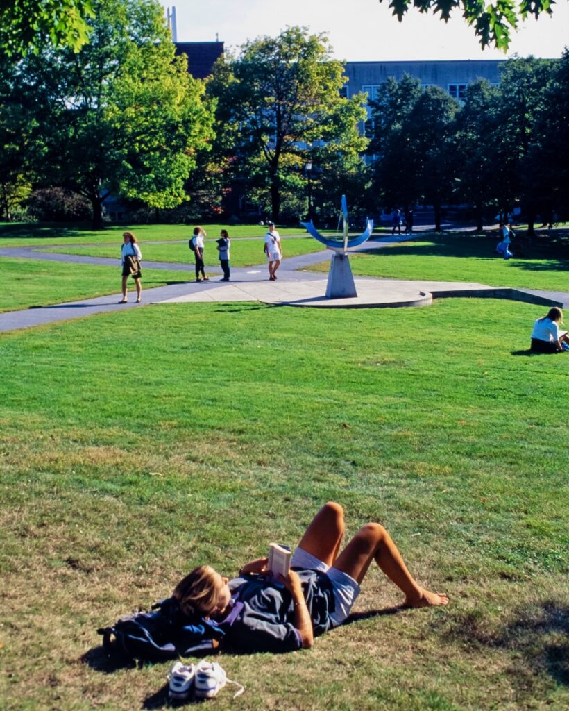 a student relaxes in the grass, with the sundial visible in the distance in the 1990s