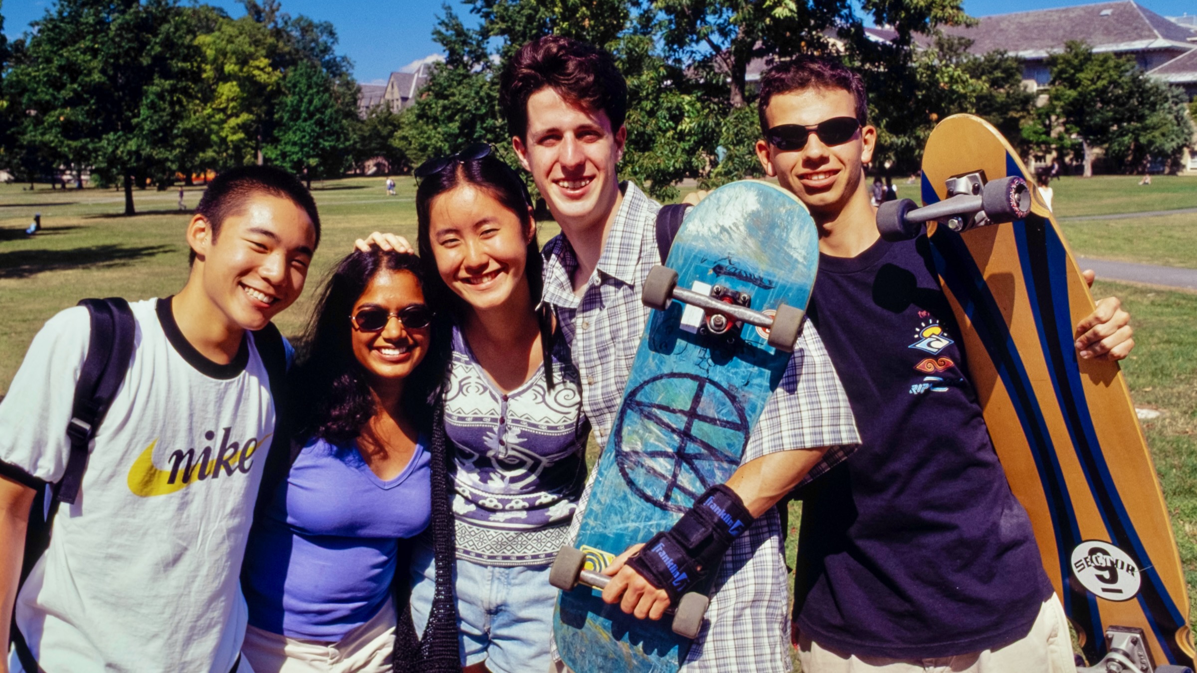 five students, two holding skateboards, pose for a photo on the Arts Quad in 1998