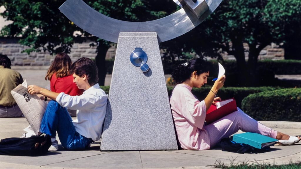 two students sit and read on opposite sides of the base of the sundial on campus in a vintage color photo from the 1990s