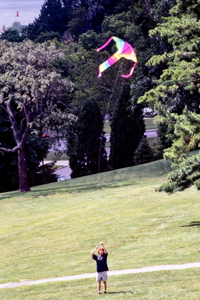 a student flies a kite on Libe Slope with a sliver of Cayuga Lake visible in the far background in a vintage color image from 2000