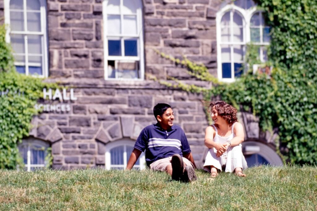 two students sit in the grass on the Arts Quad with one of the Old Stone Row buildings behind them in a vintage color image from 2000