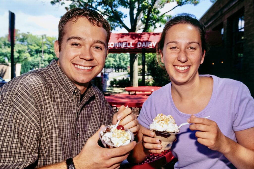 two Cornellians enjoy ice cream outside the old Cornell Dairy Bar with the red awning visible behind them in a vintage color image from 2000