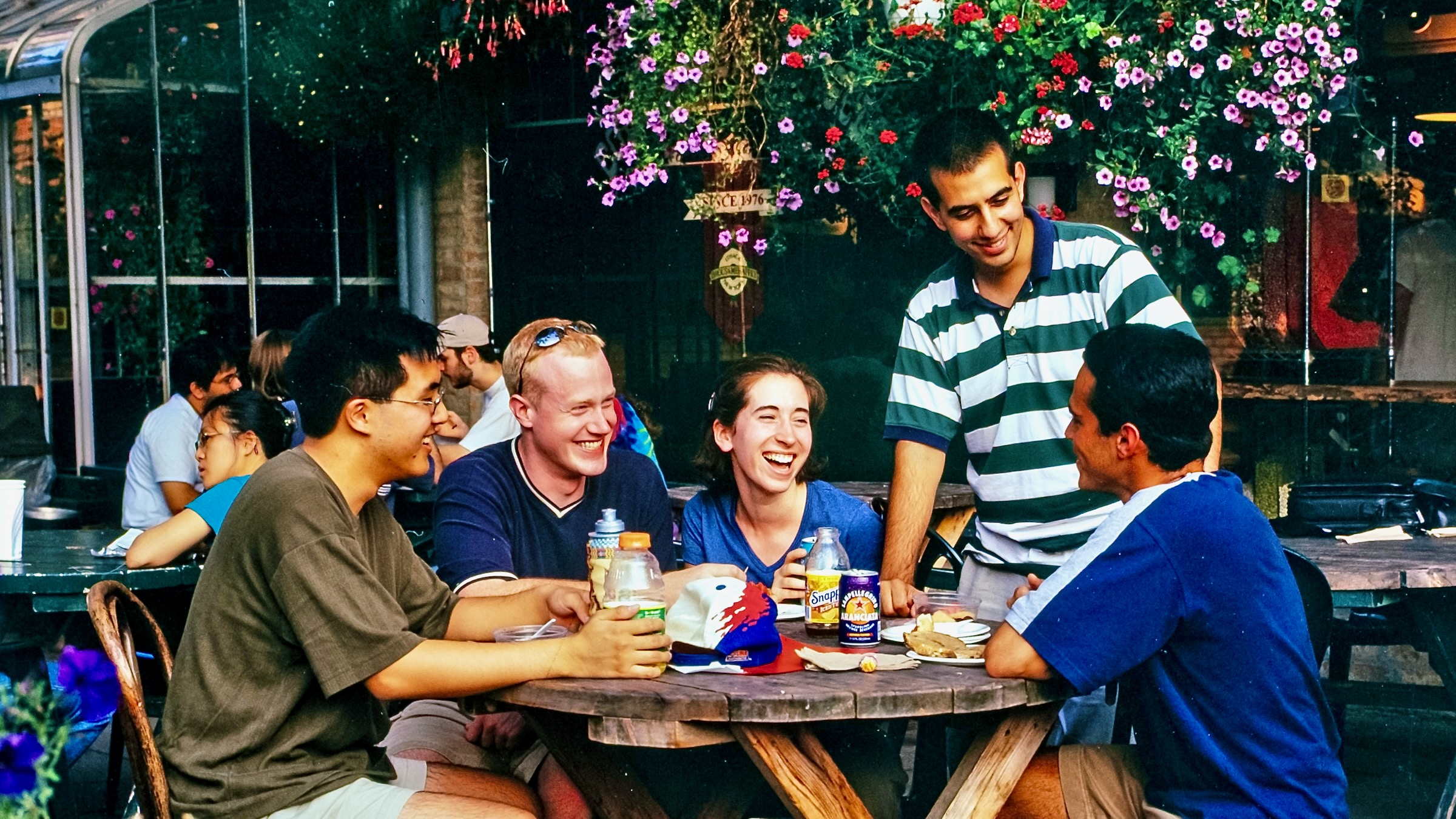 a group of students chat and laugh at an outdoor dining table at Collegetown Bagels in a vintage color image from 2000