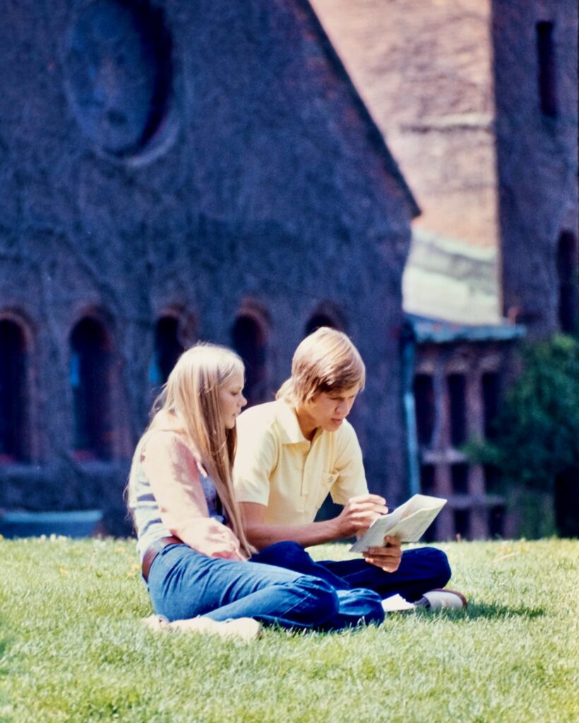 two students sit in the grass with Barnes Hall in the background in 1972