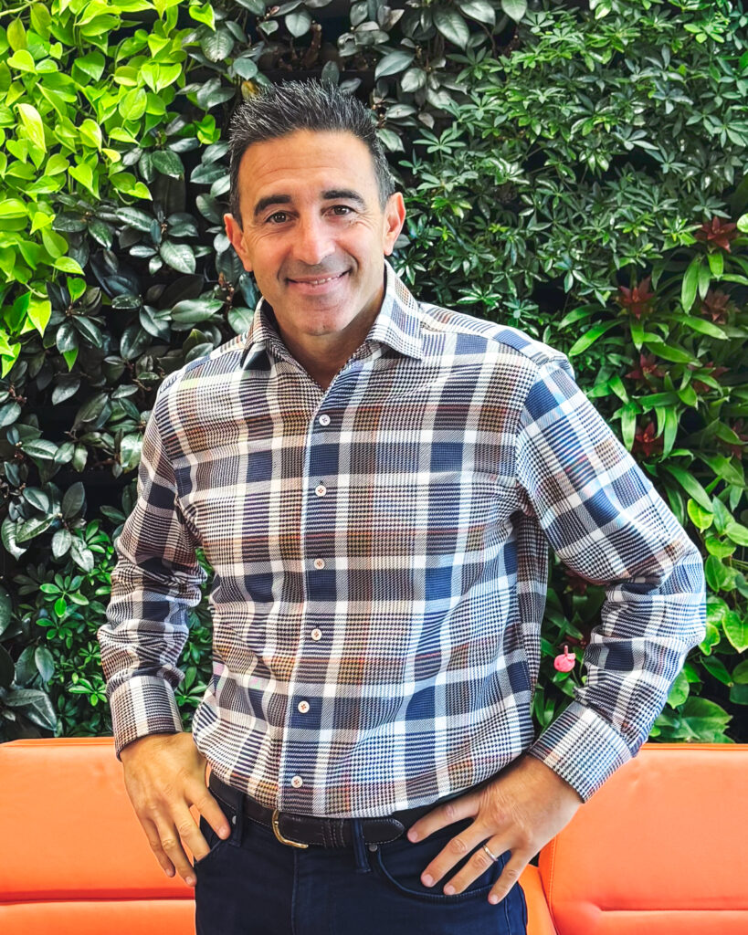 Jeremy Brunner smiles in front of a wall of greenery.