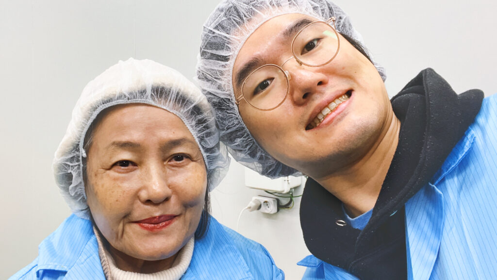 Jinhu Park with his mom, both wearing shower caps and blue coveralls