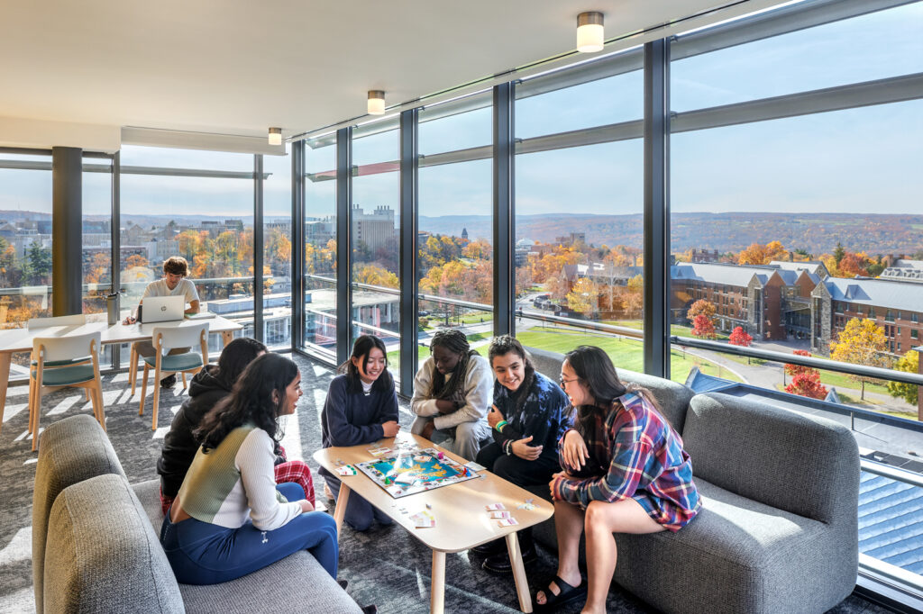 Photo by Brad Feinknopf ’86 of students in a shared space in one of the new North Campus residence halls at Cornell with large windows overlooking the rest of campus