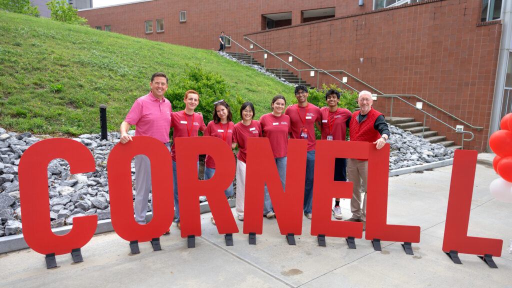 SCL VP Ryan Lombardi and President Mike Kotlikoff pose with students in red t-shirts in front of large red letters spelling CORNELL
