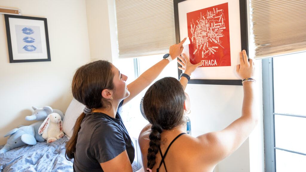 Two new students hang a framed map of Ithaca on a dorm wall