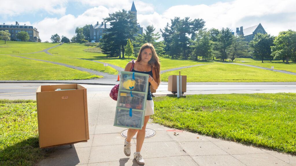 a student, carrying a set of drawers, heads toward West Campus during Move In, August 2026
