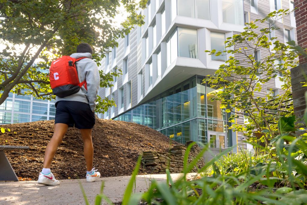A student wearing a red Cornell backpack walks up the pathway toward Upson Hall