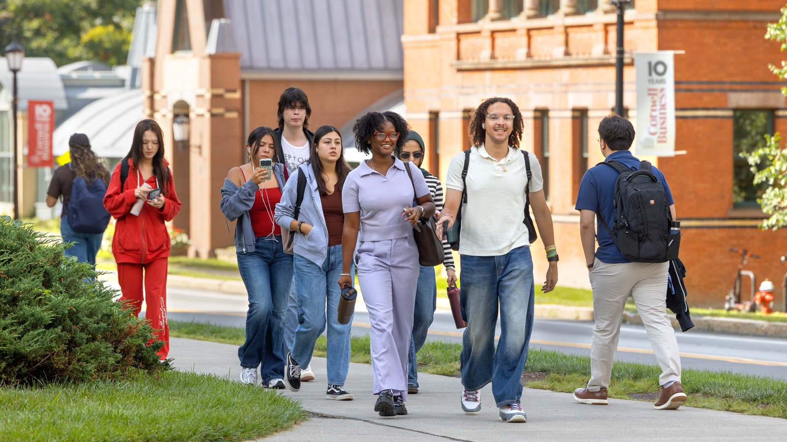 A group of smiling students walking through campus together with Sage Hall behind them