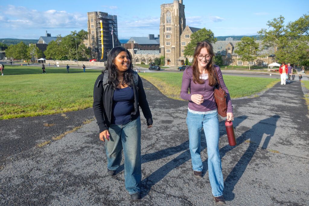 Two students smile while talking together as they walk along the Slope from West Campus