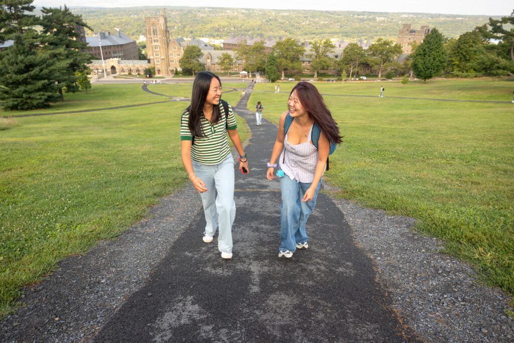 Two students smile while talking together as they walk up the Slope from West Campus