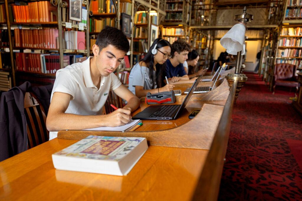 Students do work on their laptops as they sit at a table in the A.D. White Reading Room in Uris Library