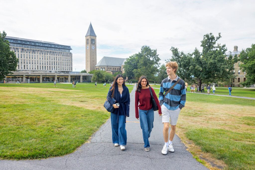 Three students smile and talk to each other while they walk through the Arts Quad