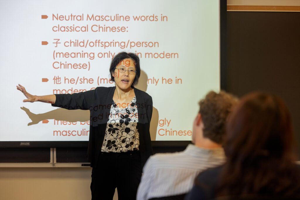 A professor stands in front of a presentation screen about Chinese language vocabulary during a class and talks to the students