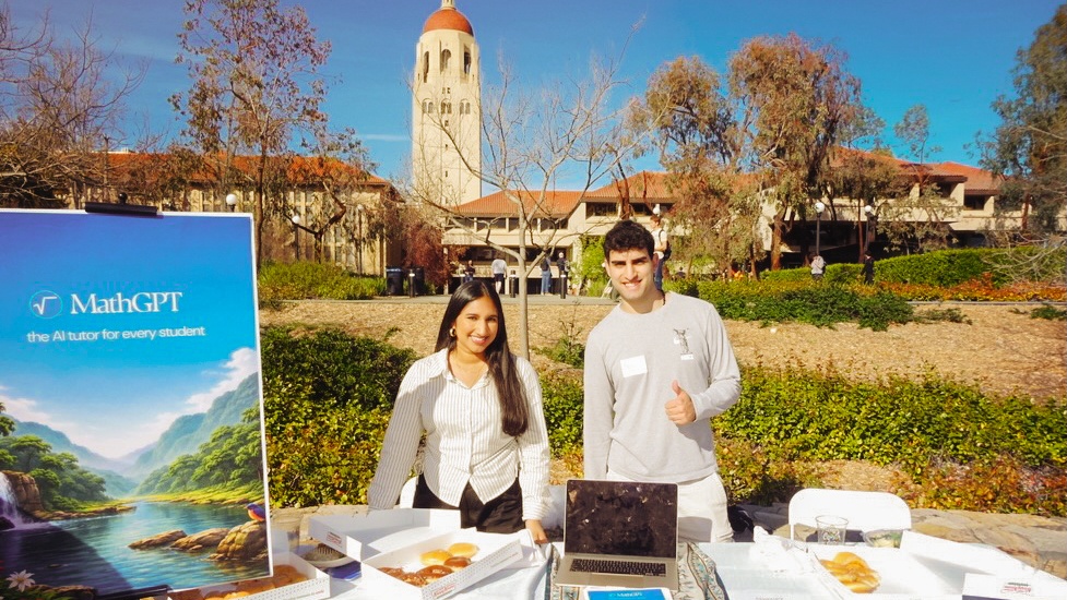 Nour Gajial and Yanni Kouloumbis outdoors on campus behind a table marketing MathGPT with a box of donuts.