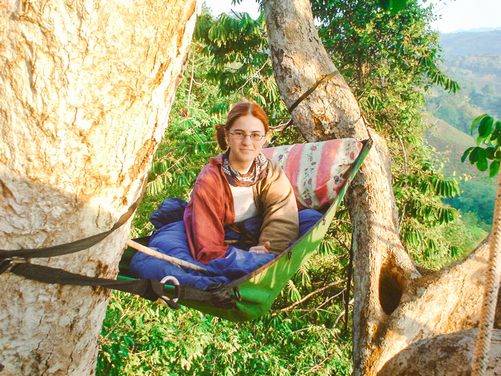 A girl sits in a hammock in the trees.
