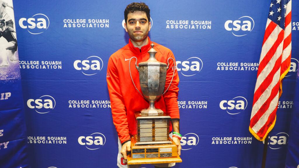 Veer Chotrani smiles with a large trophy in a Cornell Squash sweatshirt.