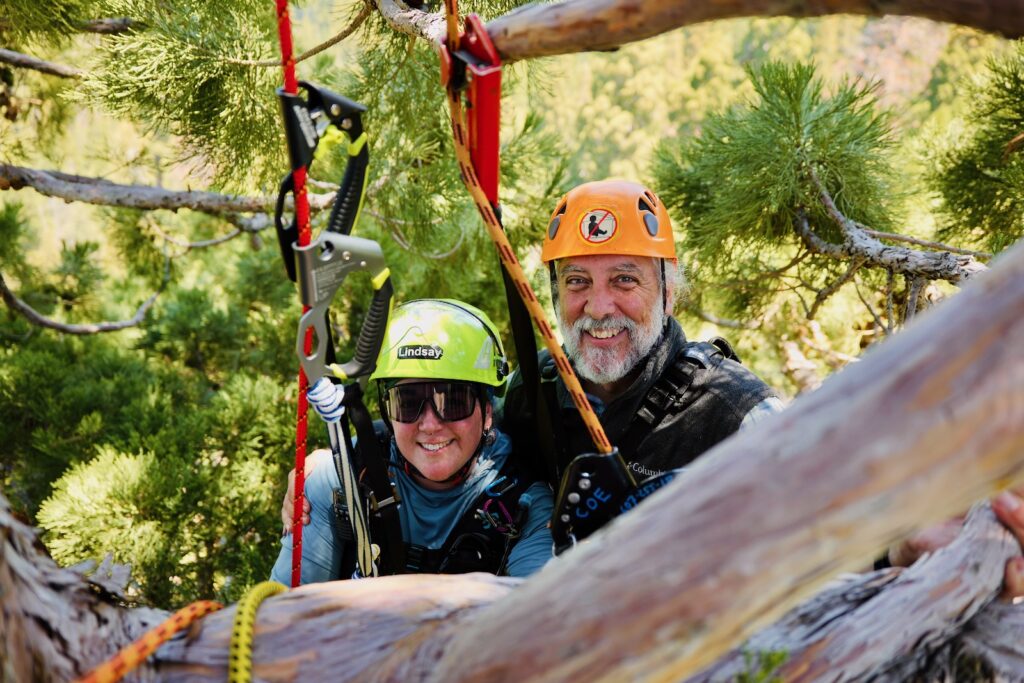 Mark Holton and Lindsay Watkins smile for a photo together in their helmets and harnesses while climbing.