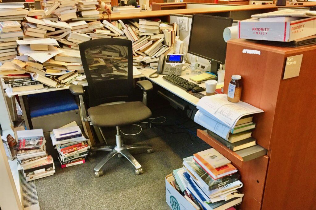 Sam Roberts's desk at the NY Times, covered in large piles of books