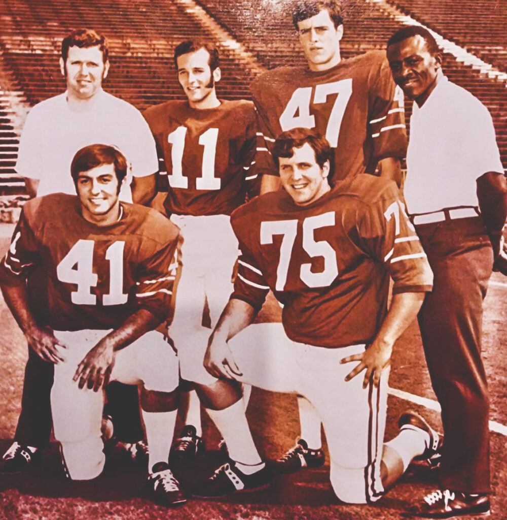 Jack Corrigan and three other Cornell football players in their uniforms with two coaches sole for a photo