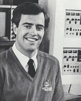 Jack Corrigan smiles while wearing a white dress shirt and tie with a sweater over it.