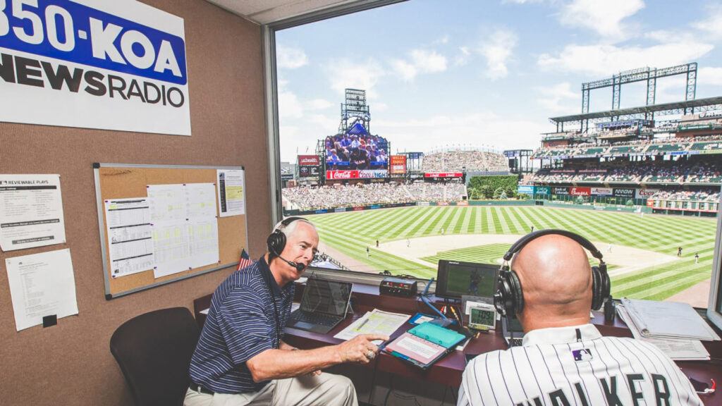 Jack Corrigan in the broadcast booth over looking the baseball stadium with Larry Walker.