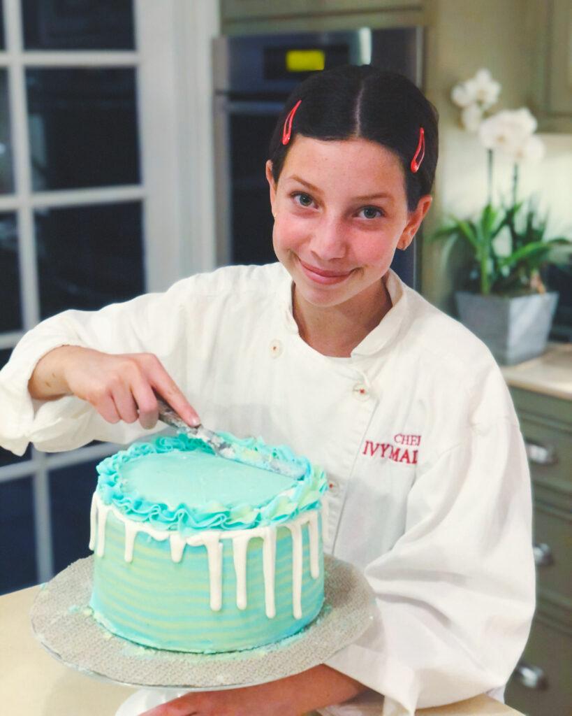 Ivy Woolenberg as a tween in chef's whites icing a blue cake