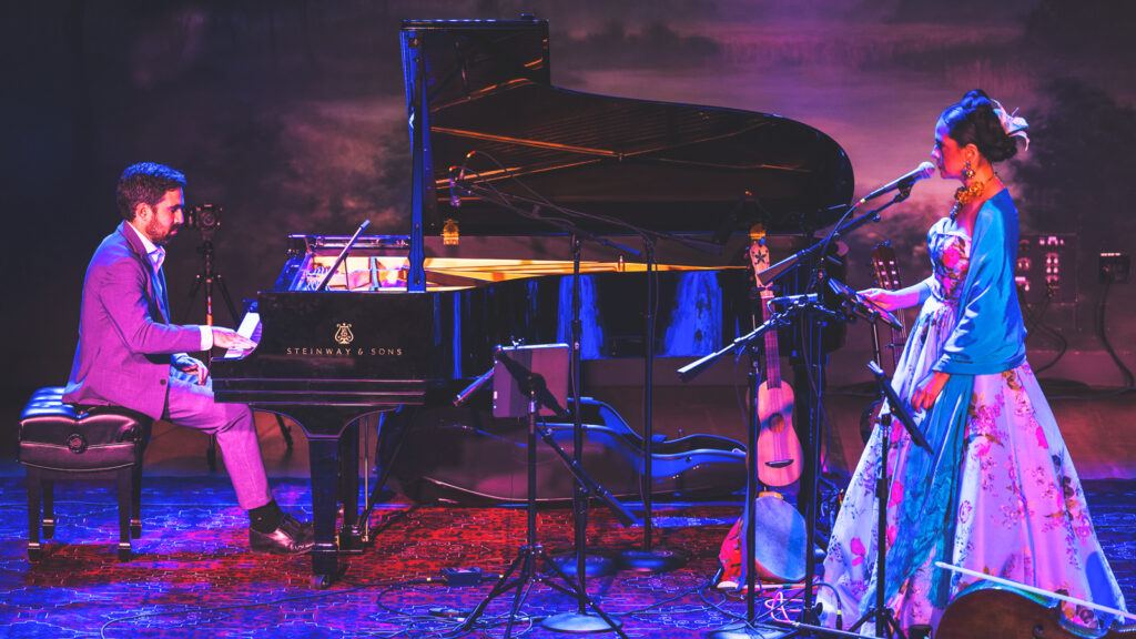 Daniel Anastasio on stage playing a piano while a singer in a large dress faces him.