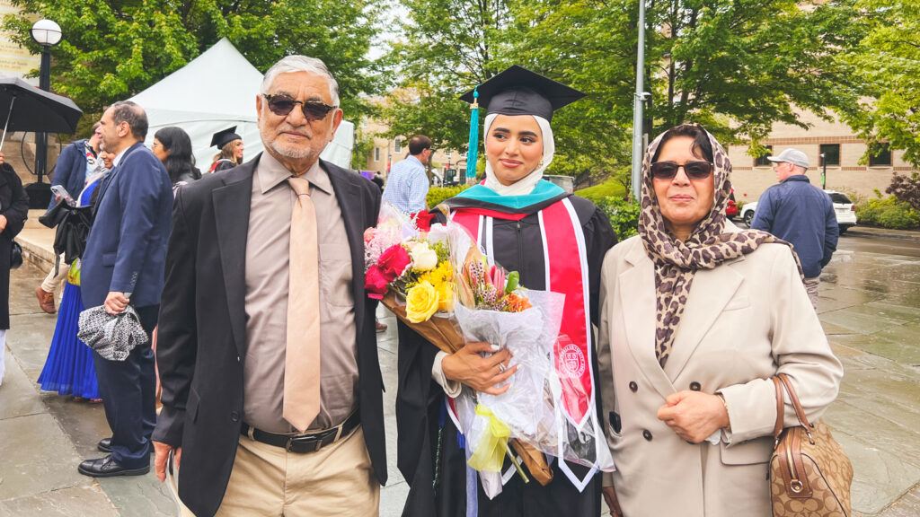 Mursal Rahim holds flowers in her regalia at graduation with her parents.