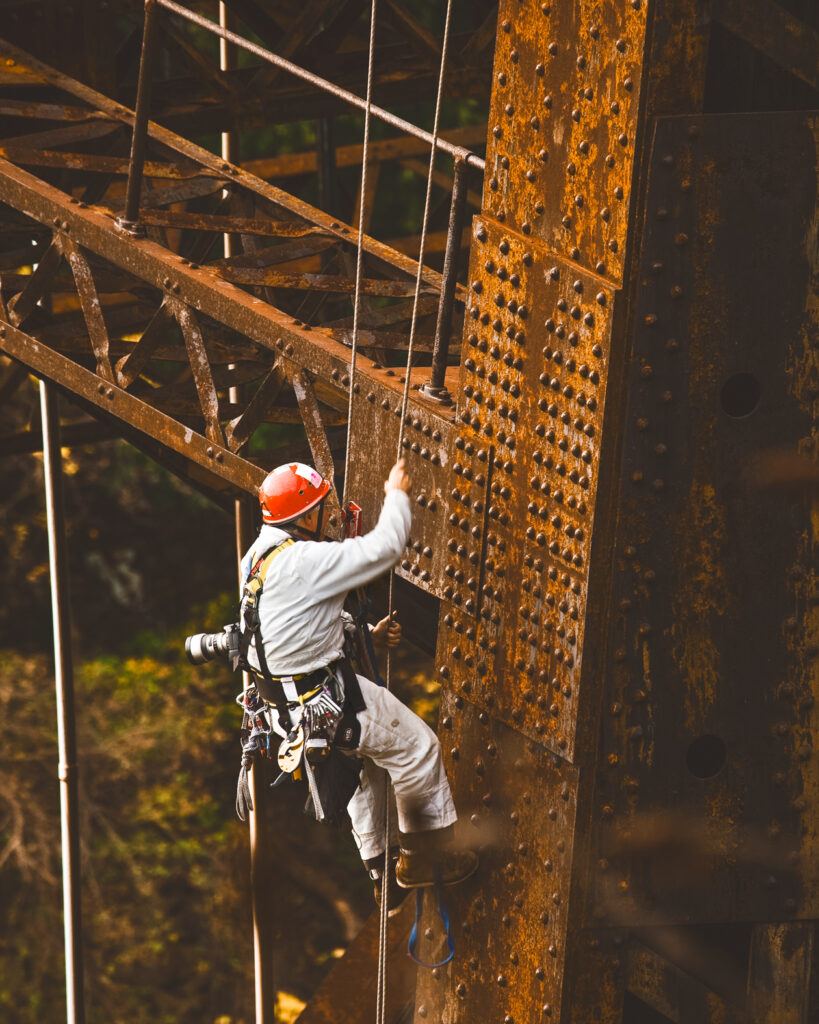 Kent Diebolt with a helmet and harness attached to climbing ropes on the side of the Canadian Pacific Railway Bridge.