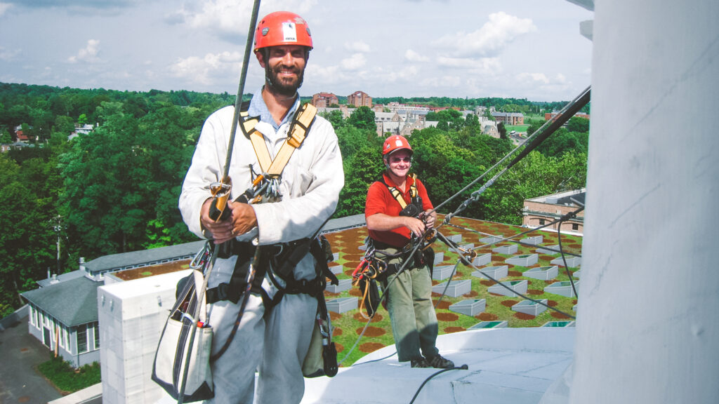 Evan Kopelson stand on the Sibley Hall Dome wearing a helment and harness with ropes attached.