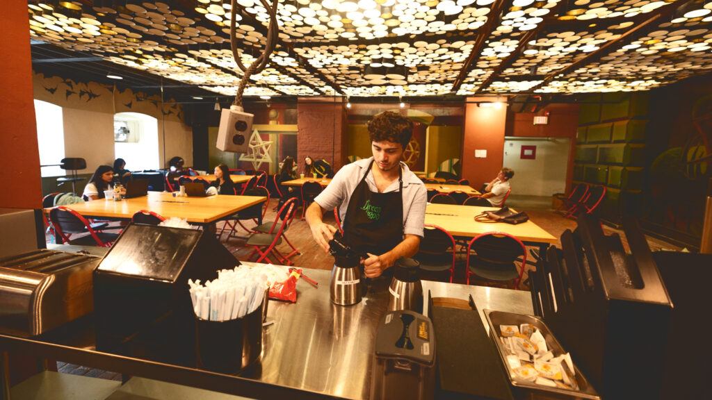 a student worker refills coffee creamer in the reopened Green Dragon Café in the lower level of Sibley Hall in 2026