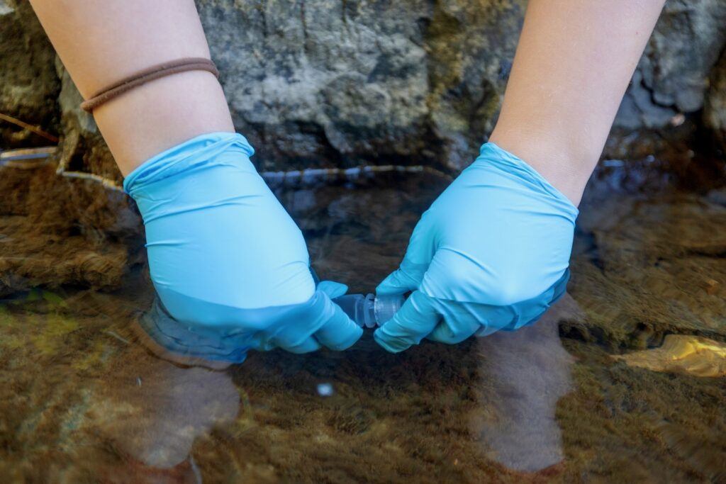 A student wearing a pair of blue latex gloves takes a water sample