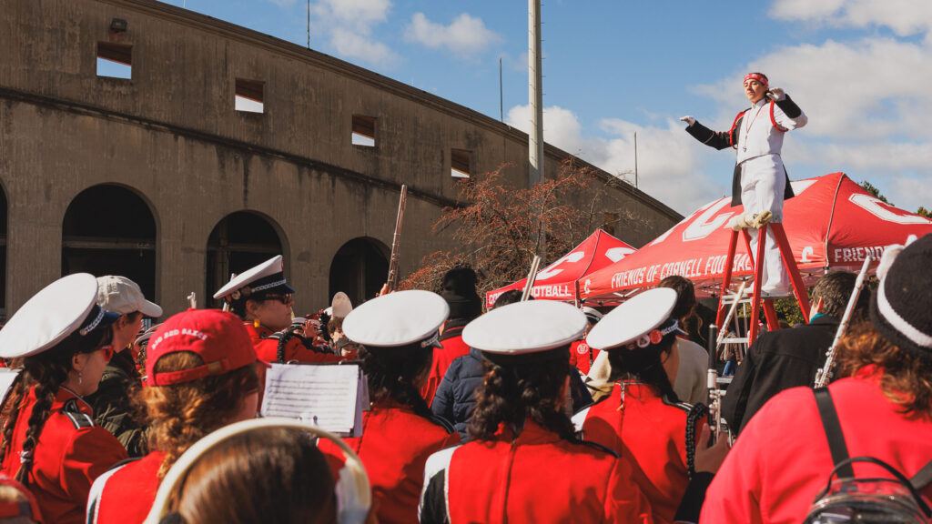 The Big Red Marching Band conductor stands on a ladder in front of the band as they prepare to play.
