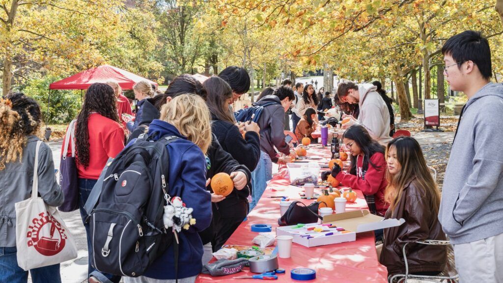 Cornell students and visitors paint mini pumpkins as part of a fall-themed Homecoming Weekend event on Ho Plaza