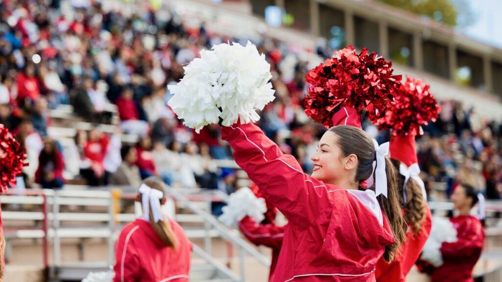 A Cornell cheerleader smiles and waves white and red pompoms in the air.