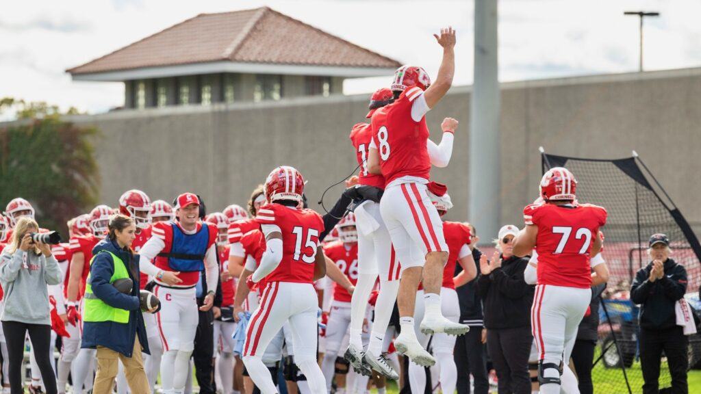 Cornell players jump in the air and celebrate together on the sideline.