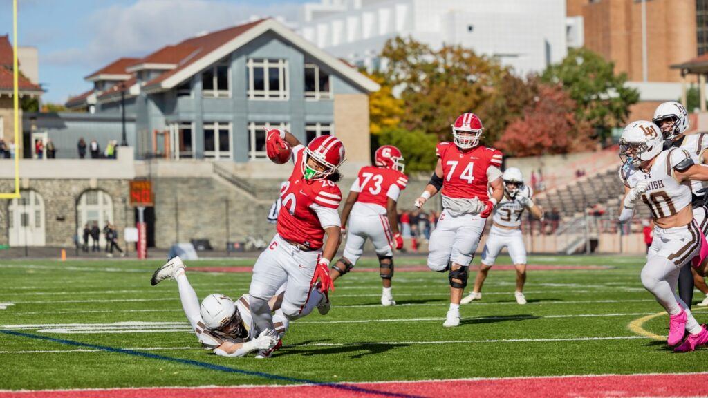 A Cornell football player runs with the ball while a Lehigh player attempts a tackle
