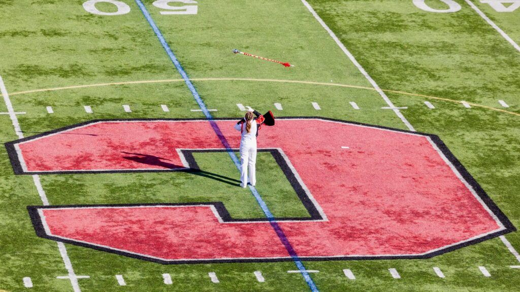 A member of the Cornell marching band throws the baton in the air while standing in the center of the football field.