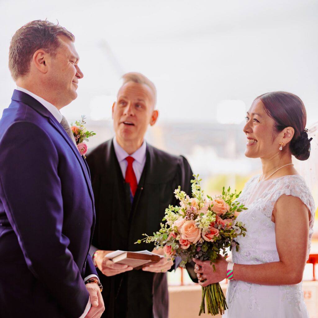 Yuko Jingu and Jeffry Clausen Jr. smile at each other while being married by Tompkins County Judge Scott Miller.