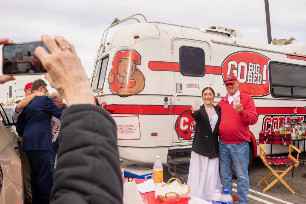 Yuko Jingu and Dan Dwyer smile for a photo while holding their drinks in the air in front of the “Spirit of ’76” van.