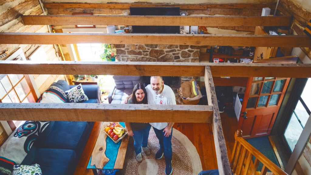 Jen Riley and Michael Oak stand in their living room, viewed from above from their cabin's half-loft
