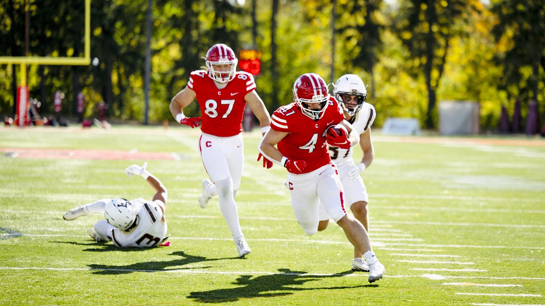 A Cornell player runs the football down field with another teammate while a Lehigh player chases behind him.