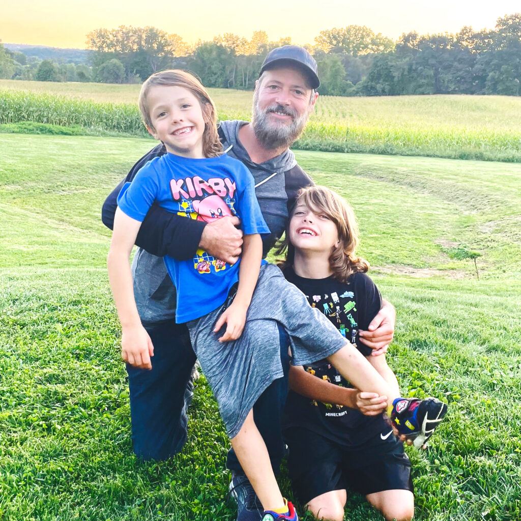 Alex Colket holding his young nephews in a green field