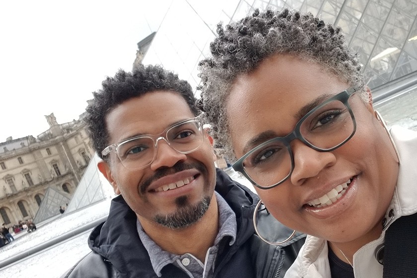 Close-up of a couple with the glass pyramid entrance of the Louvre in the background