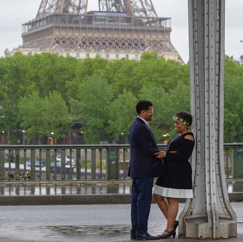 A well-dressed couple on a rainy morning with the Eiffel tower base in the background.
